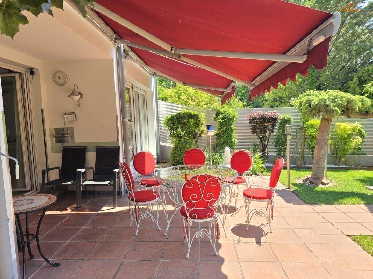 Gemütliche Terrasse mit roter Markise, Gartenmöbeln und Zugang zum gepflegten Gartenbereich.