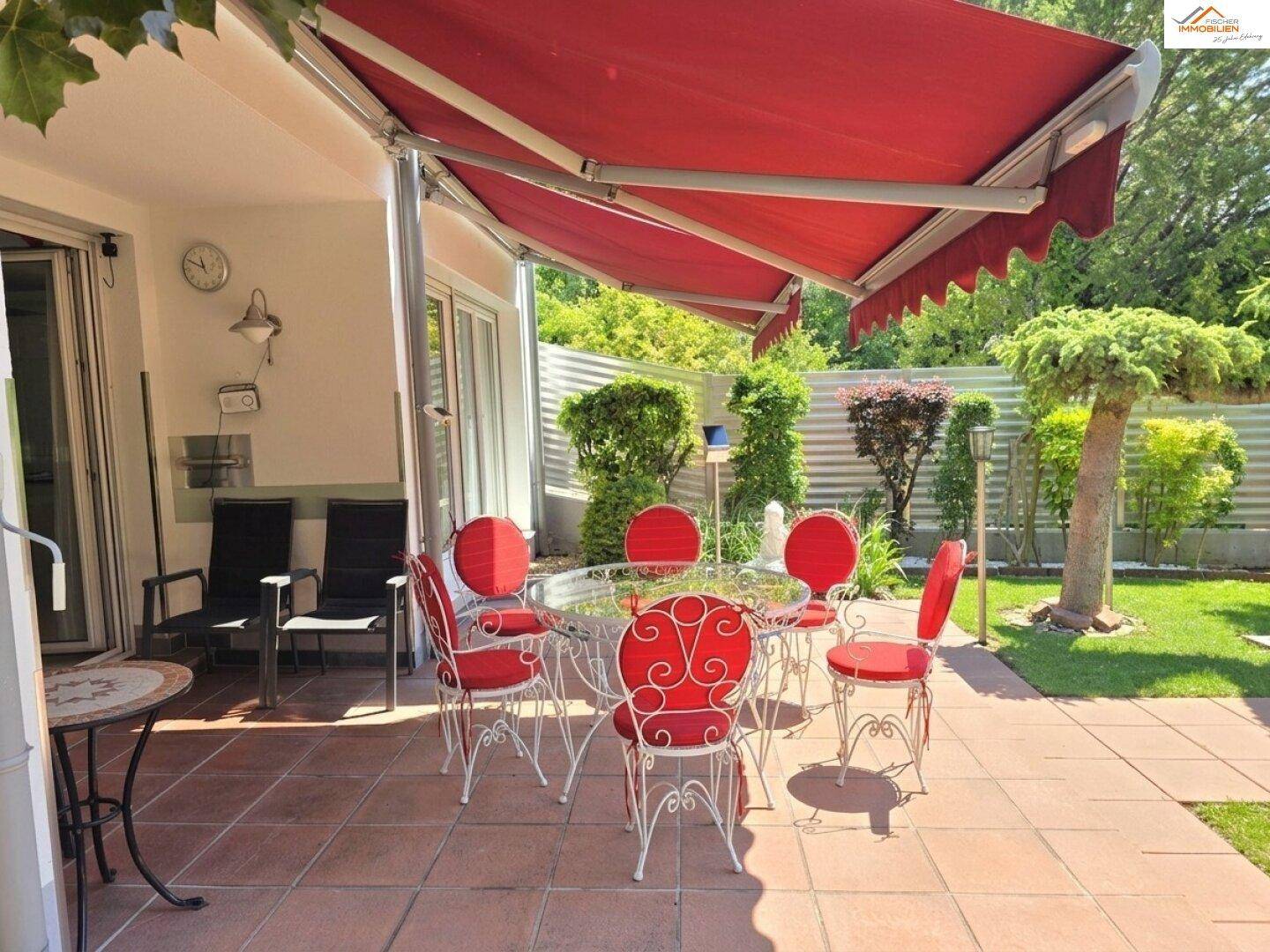 Gemütliche Terrasse mit roter Markise, Esstisch und Blick in den gepflegten Garten.