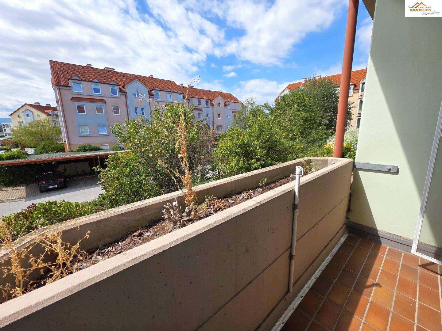 Balkon mit Blumenkasten und Blick auf die umliegenden Gebäude und Parkplätze.