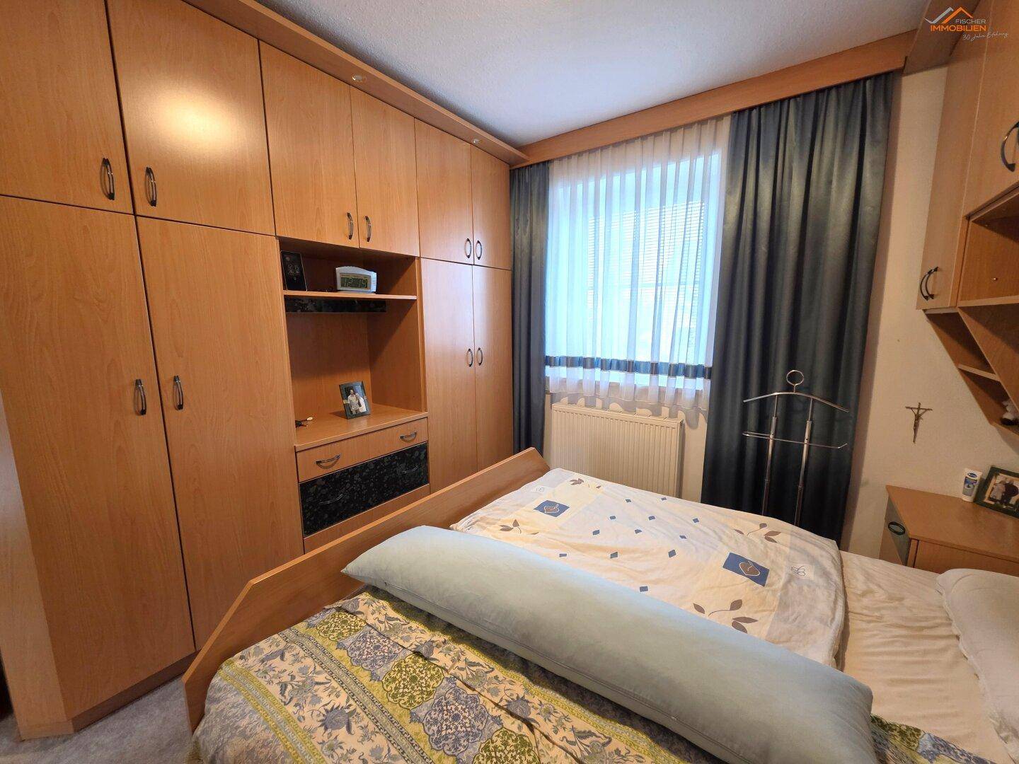 Schlafzimmer mit umfangreichen Einbauschränken aus Holz und einem großen Fenster.