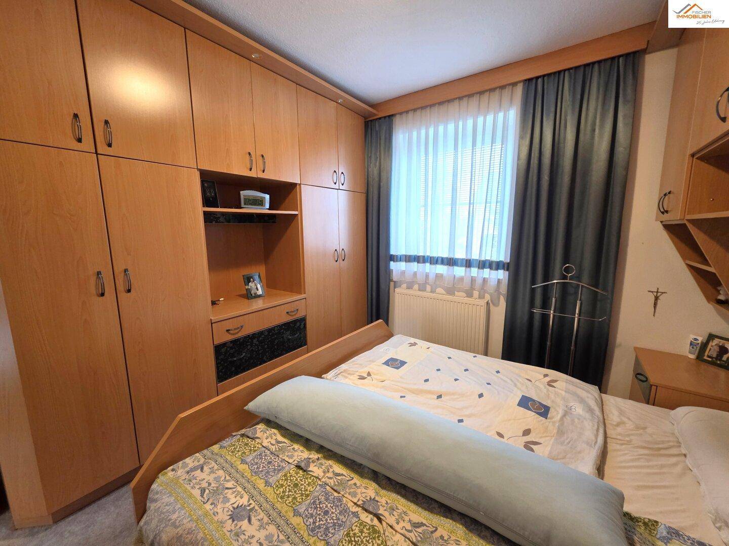 Schlafzimmer mit Einbauschränken, Doppelbett und Vorhängen, gemütlich eingerichtet.