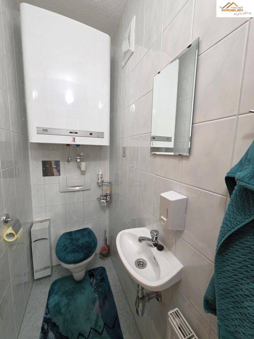Kleines Gäste-WC mit Wand-WC, Waschbecken und Boiler, hell gefliest.