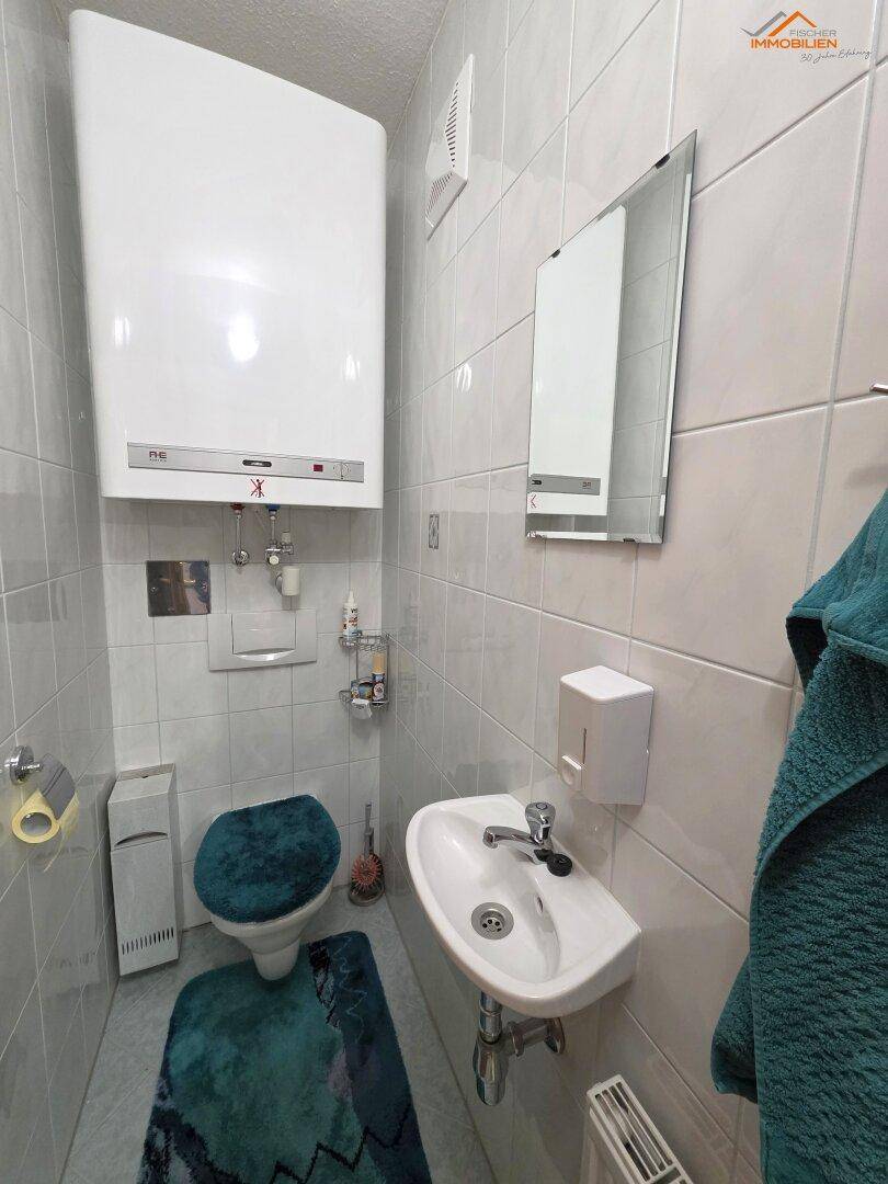 Kleines Gäste-WC mit Waschbecken, Toilette und Wandfliesen in hellem Design.