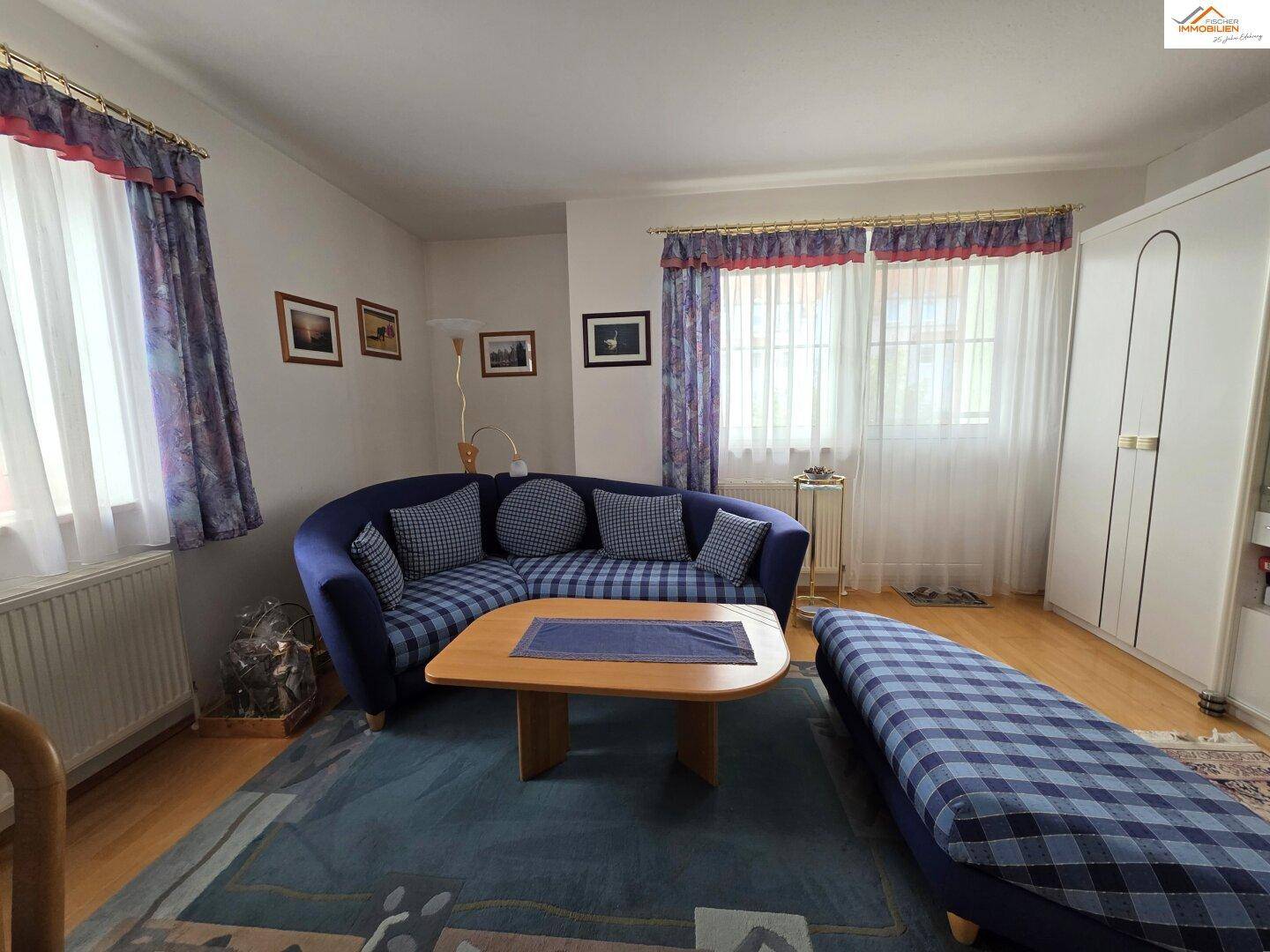 Wohnzimmer mit blauer Eckcouch, Holztisch und großem Fenster für viel Tageslicht.