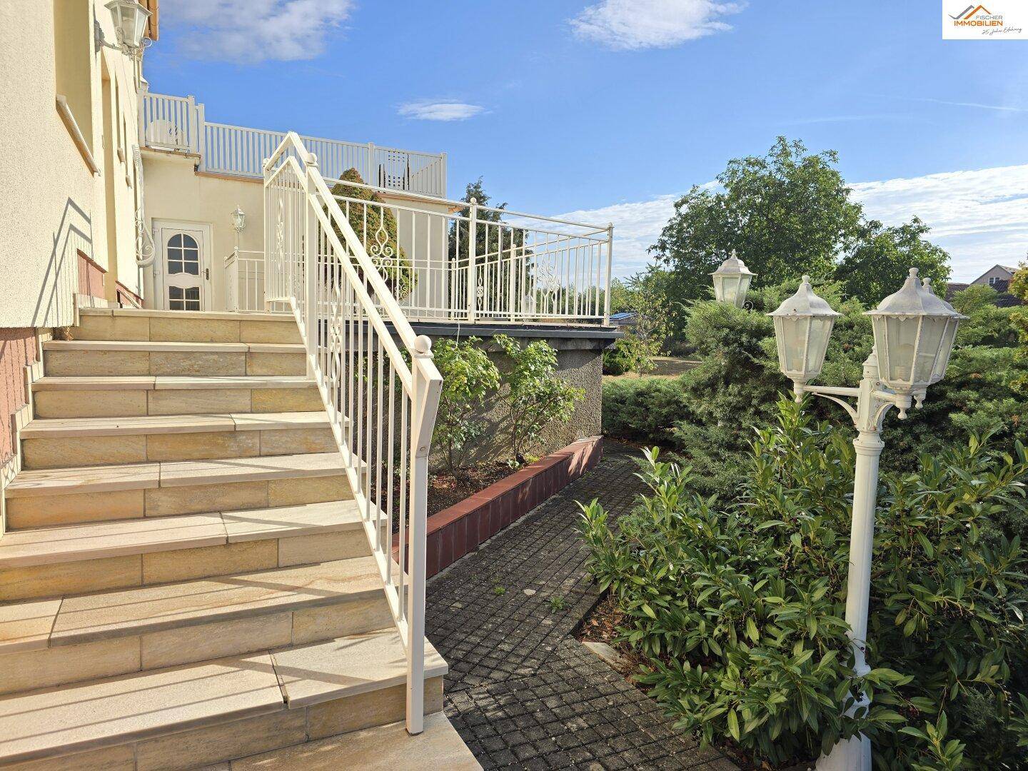 Außentreppe mit weißem Geländer führt zur oberen Terrasse und zum Eingangsbereich.