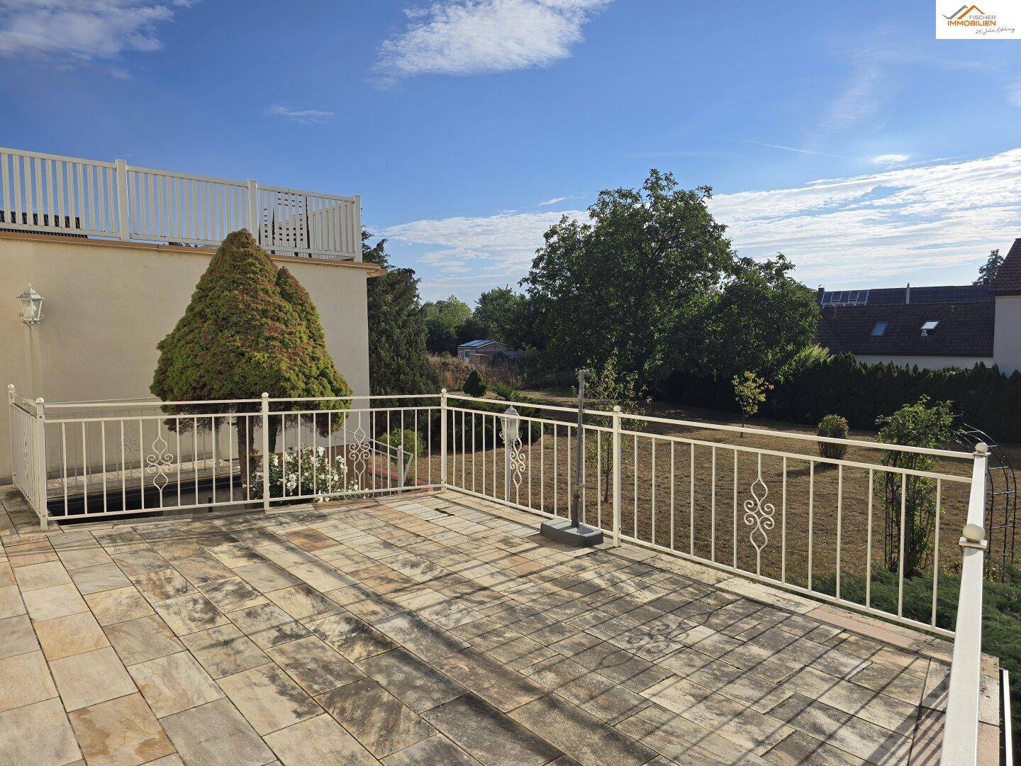 Geräumige, geflieste Terrasse mit weißem Geländer und Blick auf den Garten und die Umgebung.