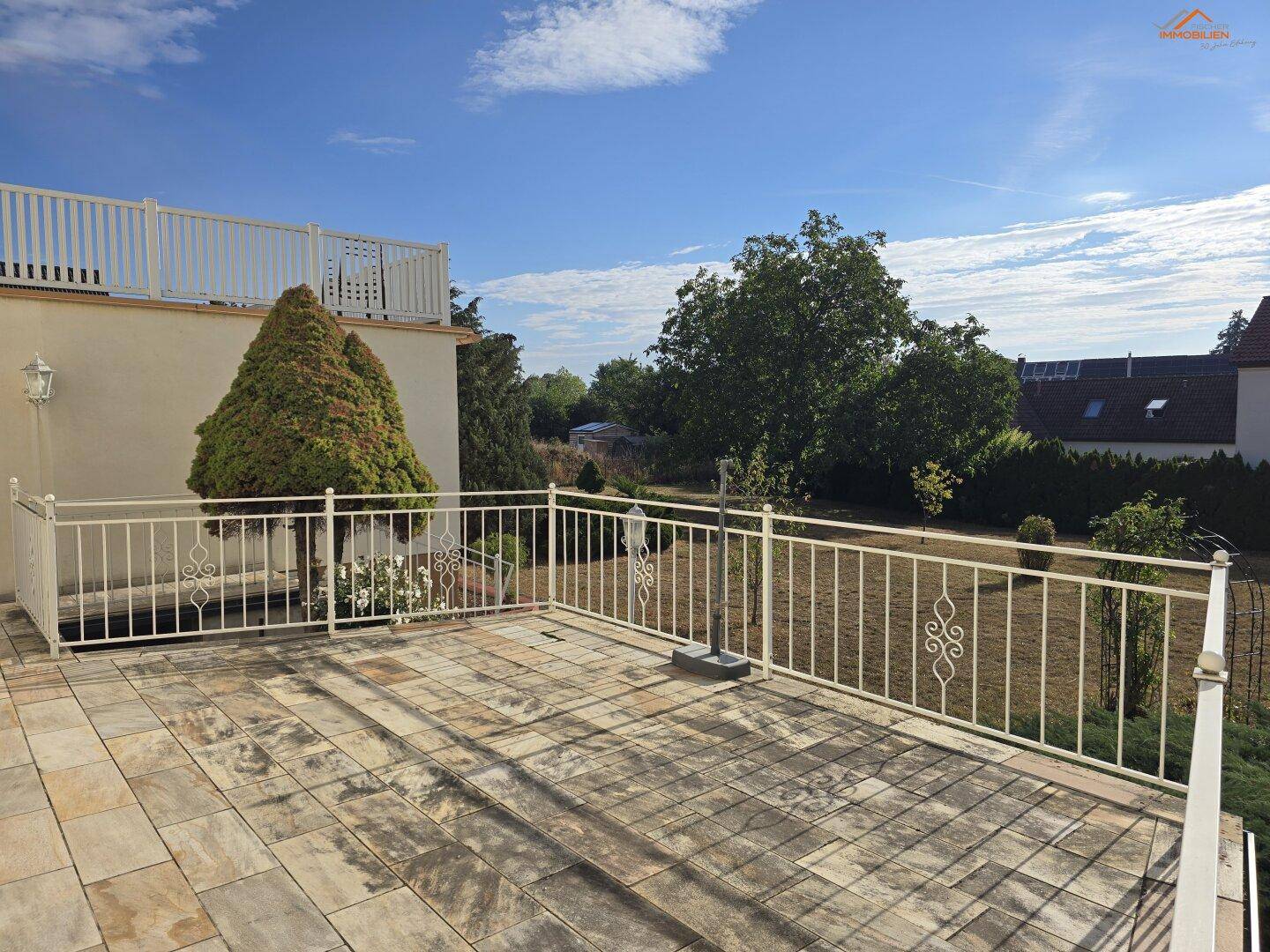 Geräumige Terrasse mit Fliesenboden und weißem Geländer, bietet weiten Blick ins Grüne.