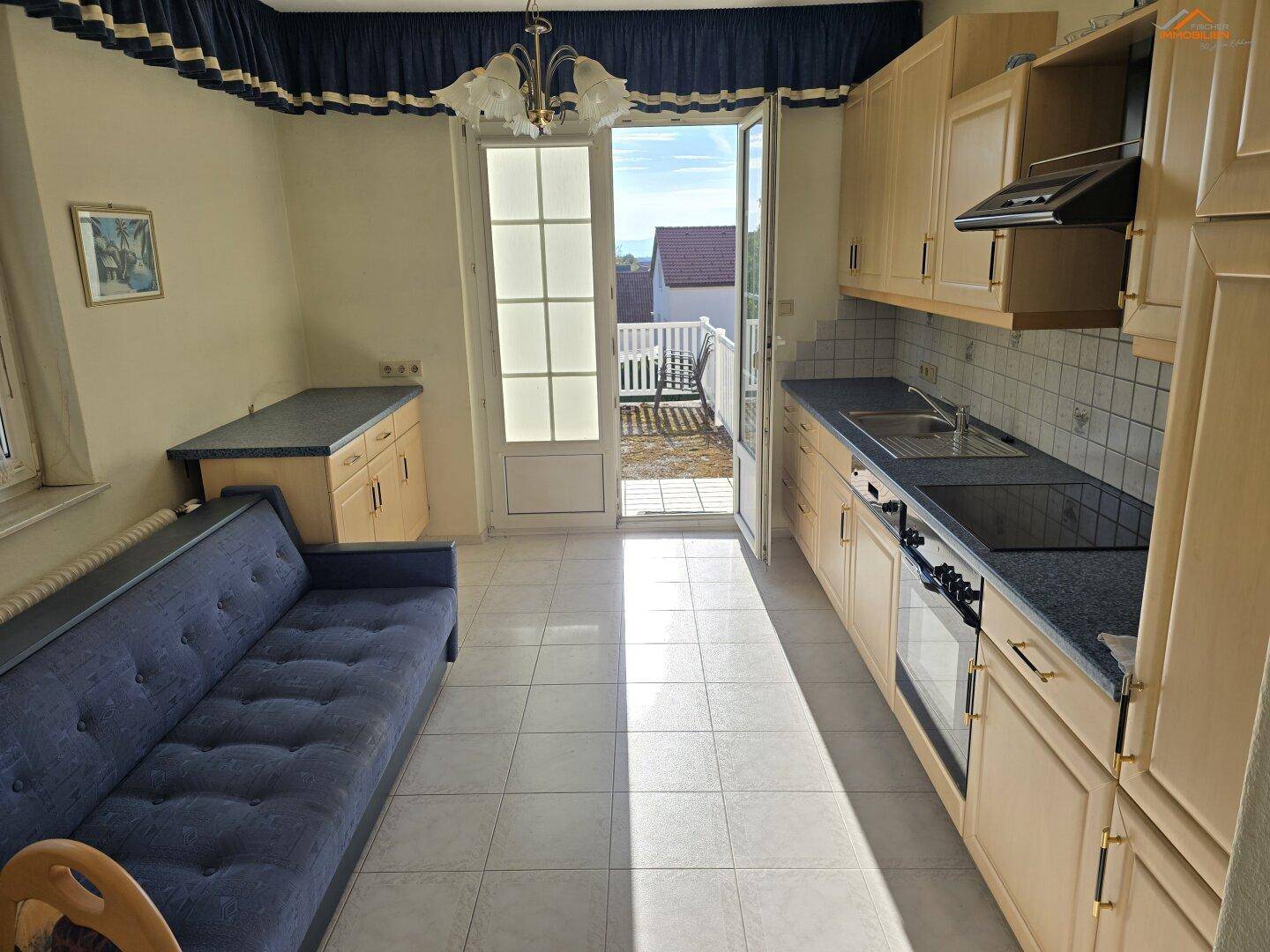 Küche mit Fliesenboden und direktem Zugang zur Terrasse, ausgestattet mit Küchenzeile und Sofa.