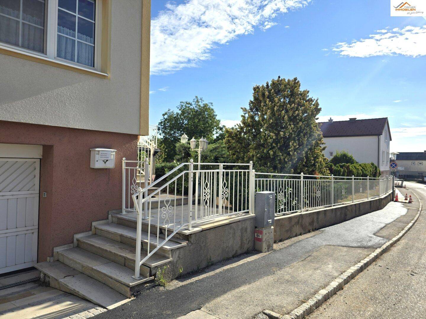 Außentreppe mit weißem Geländer und Zaun, der das Grundstück zur Straße hin abgrenzt.