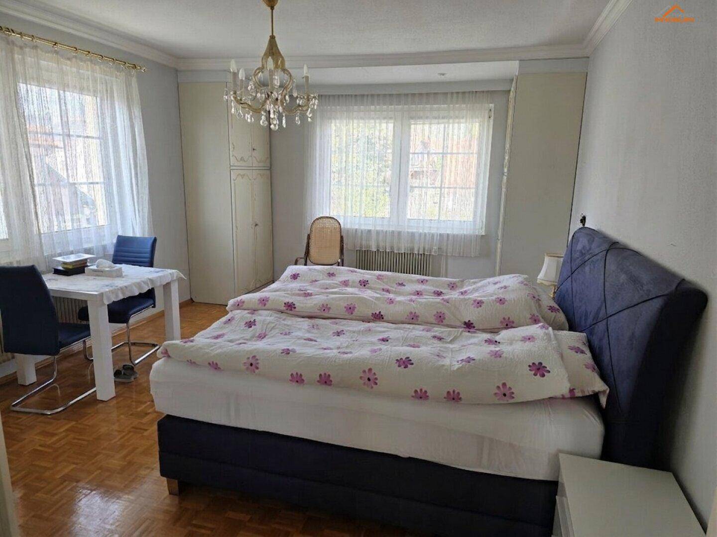 Geräumiges Schlafzimmer mit Doppelbett, Parkettboden und großen Fenstern, hell und komfortabel.
