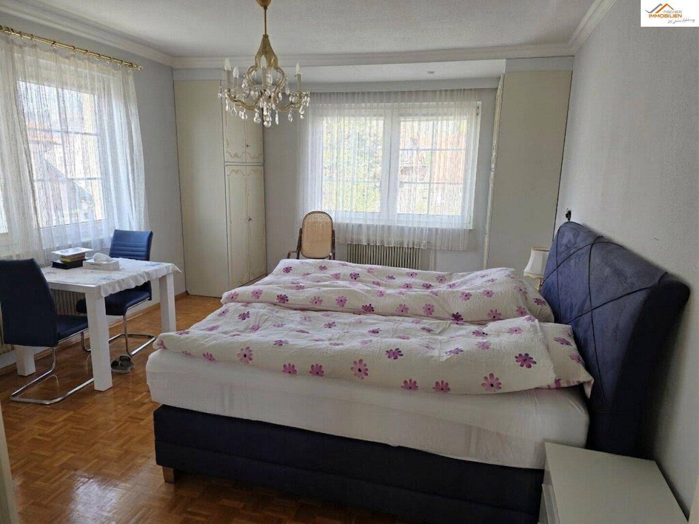 Geräumiges Schlafzimmer mit Doppelbett, Parkettboden und viel Tageslicht durch große Fenster.