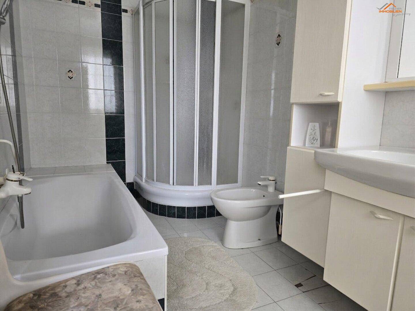 Badezimmer mit Badewanne, Duschkabine und Bidet, gefliest in hellen und dunklen Tönen.