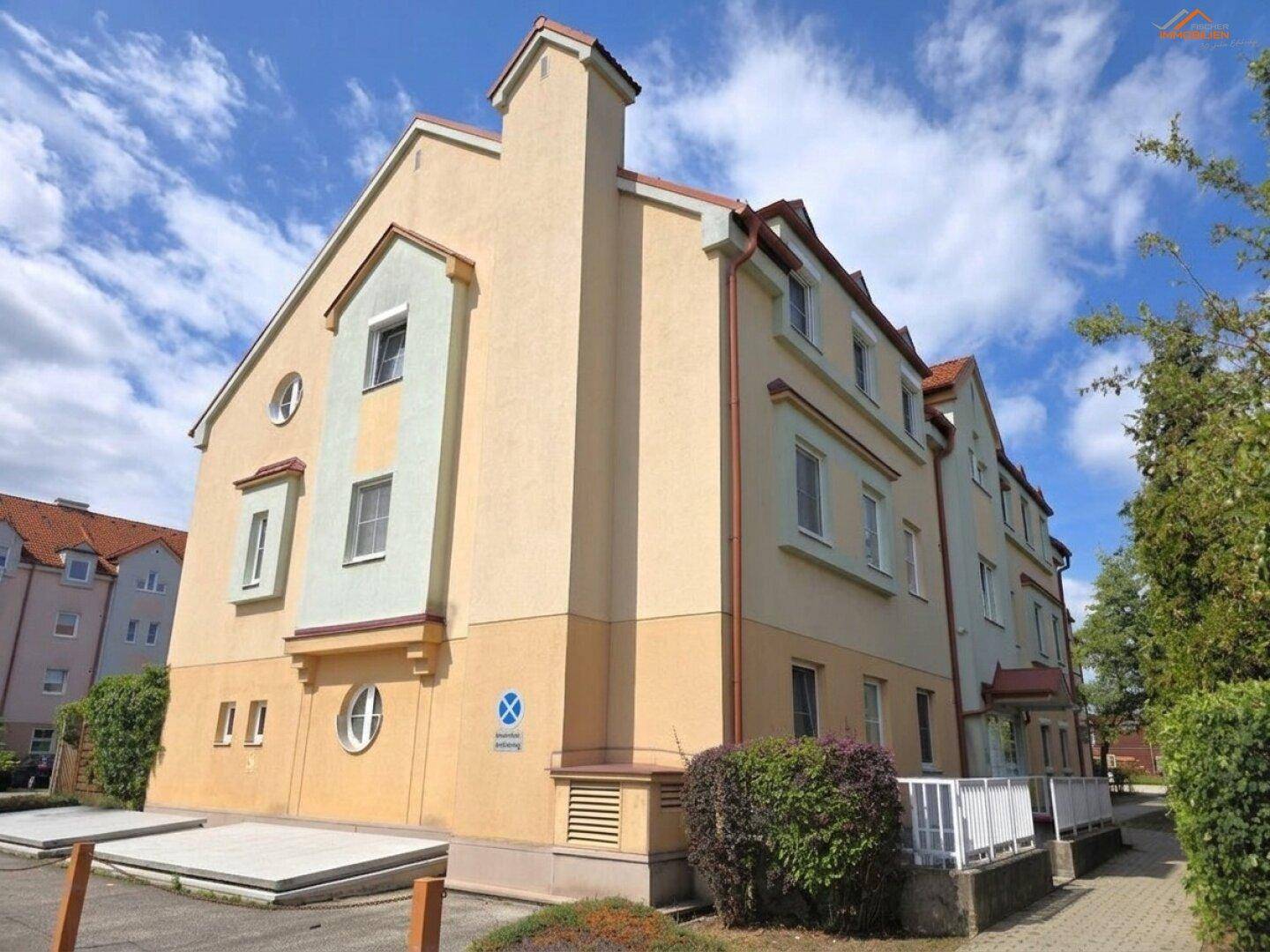 Ansicht des Mehrfamilienhauses mit farbiger Fassade, Fenstern und Zugang zum Parkplatz.
