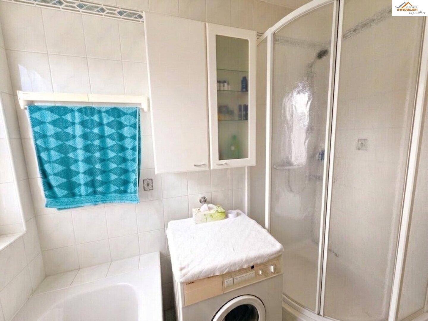 Badezimmer mit Duschkabine, Badewanne und Waschmaschine, hell gefliest und funktional.