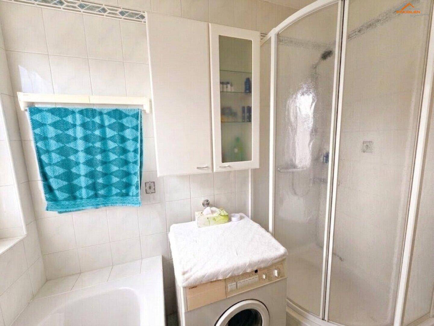 Badezimmer mit Duschkabine, Badewanne und Waschmaschine, alles in hellen Fliesen gehalten.