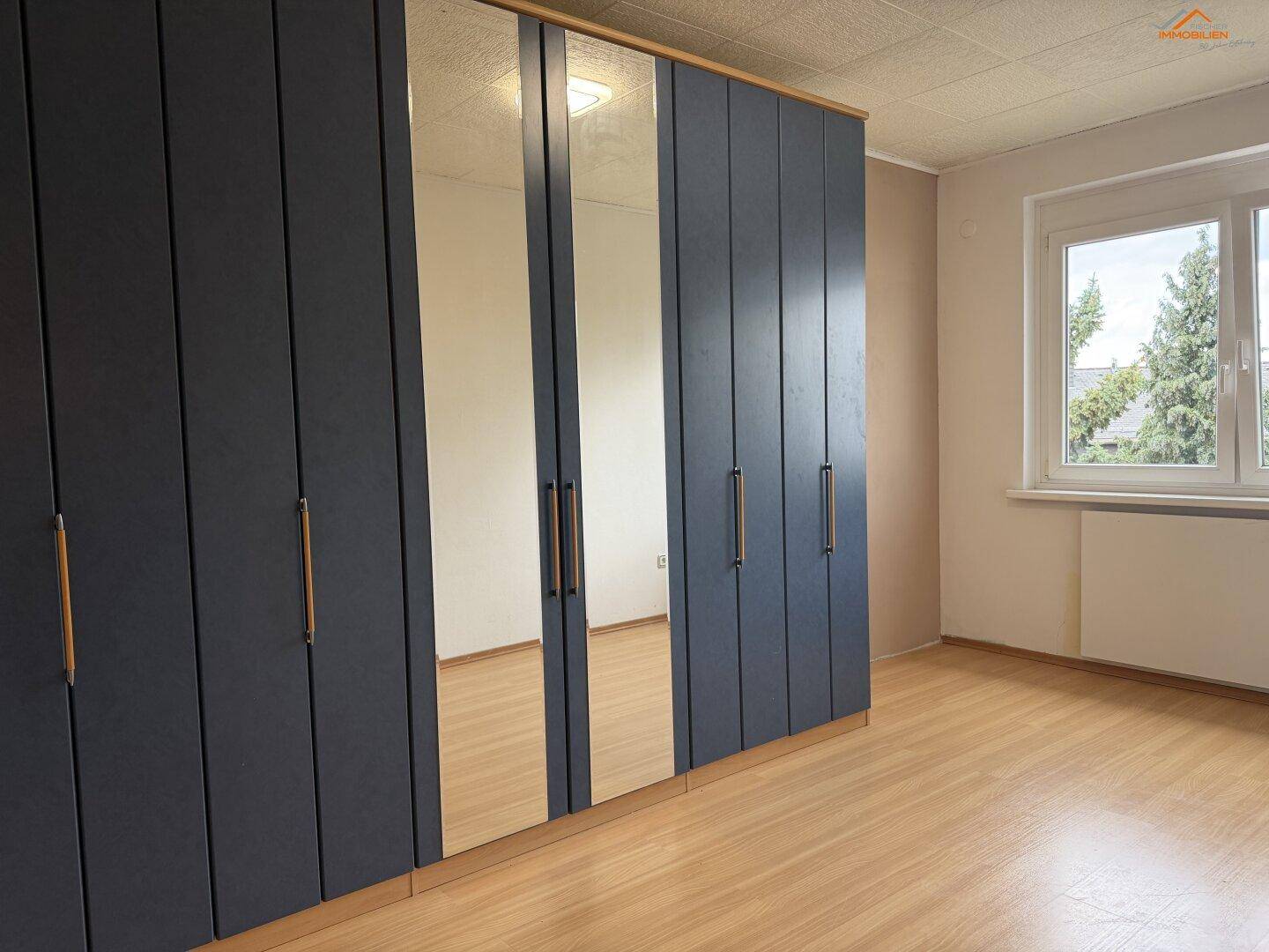 Schlafzimmer mit großen, dunkelblauen Einbauschränken, Spiegeltüren und hellem Laminatboden.