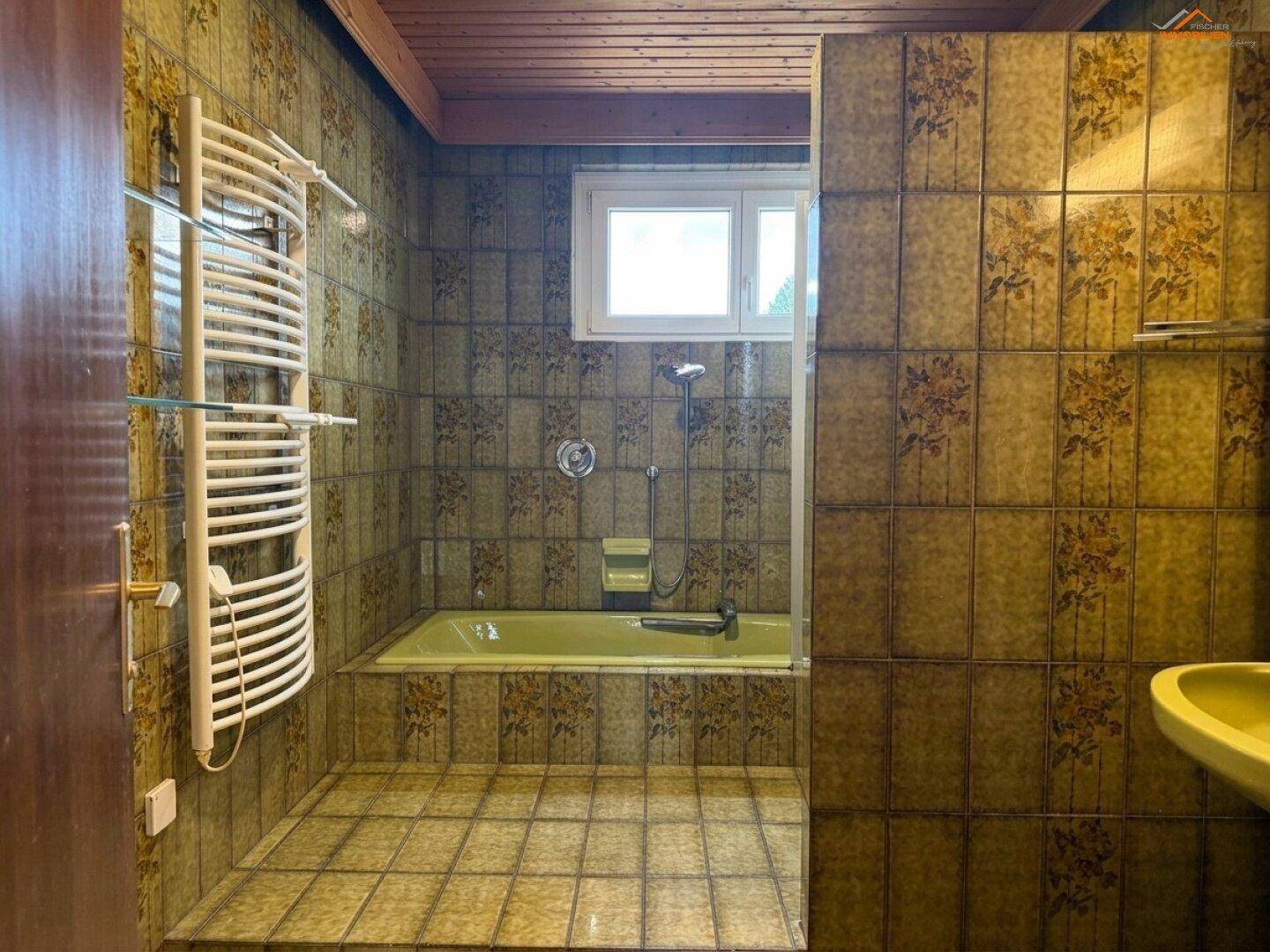 Badezimmer im 80er-Jahre-Stil mit floralen Fliesen, gelber Badewanne und beheiztem Handtuchhalter.