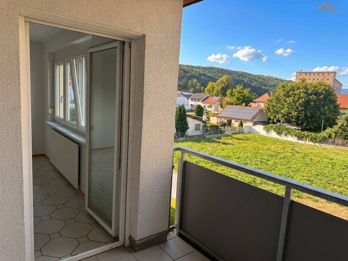Balkon mit weitem Blick über grüne Landschaft und Berge, verbunden mit einem hellen Innenraum.