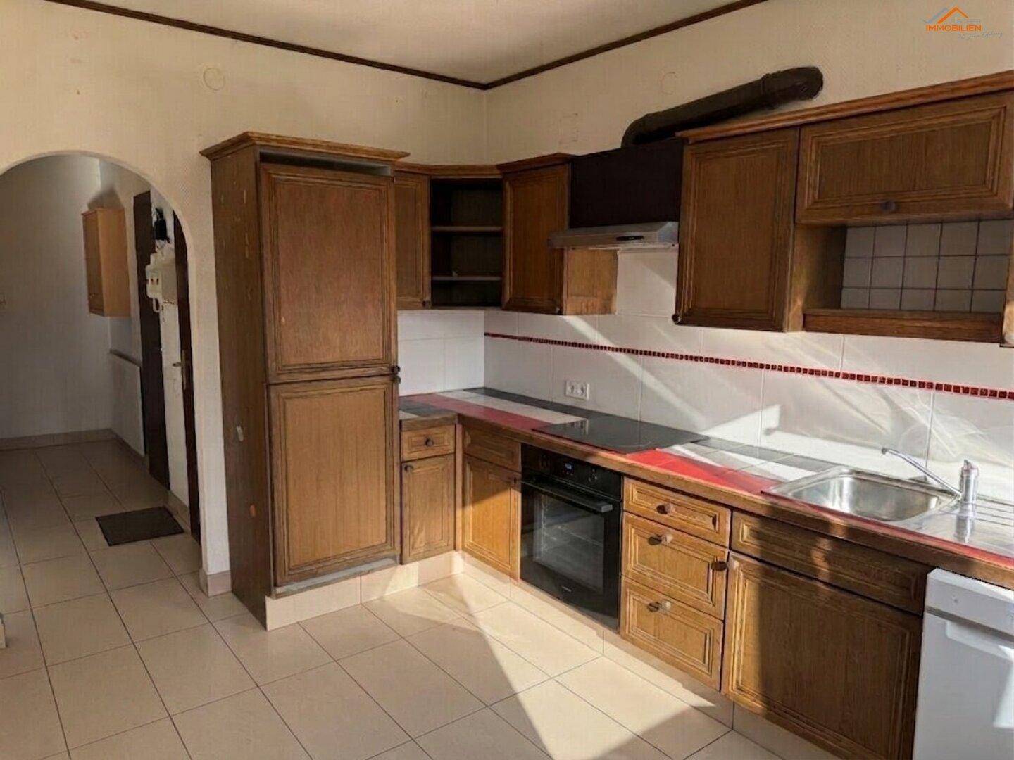 Funktionale Küche mit älteren Holzschränken, dunkler Arbeitsplatte und Fliesenboden, bereit zur Modernisierung.