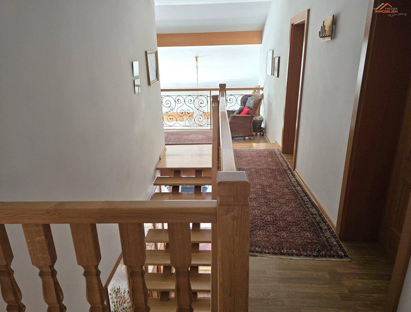 Heller Flur mit Holztreppe und Teppichläufer, der zu den oberen Etagen führt.