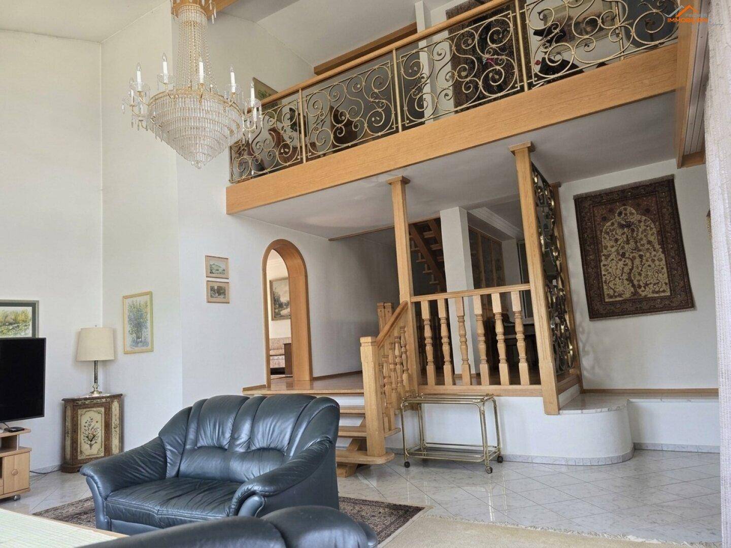 Großzügiges Wohnzimmer mit Galerie, hohen Decken und dekorativem Kronleuchter.