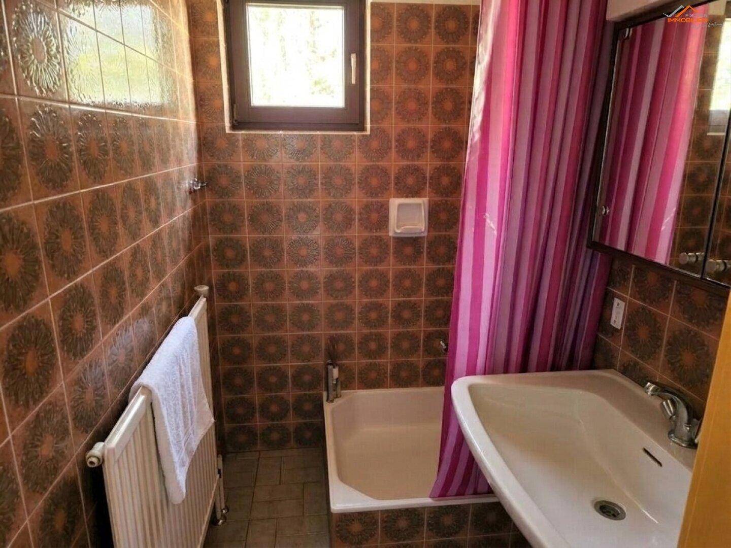Badezimmer im 80er-Jahre-Stil mit braunen Fliesen, Badewanne und Fenster.