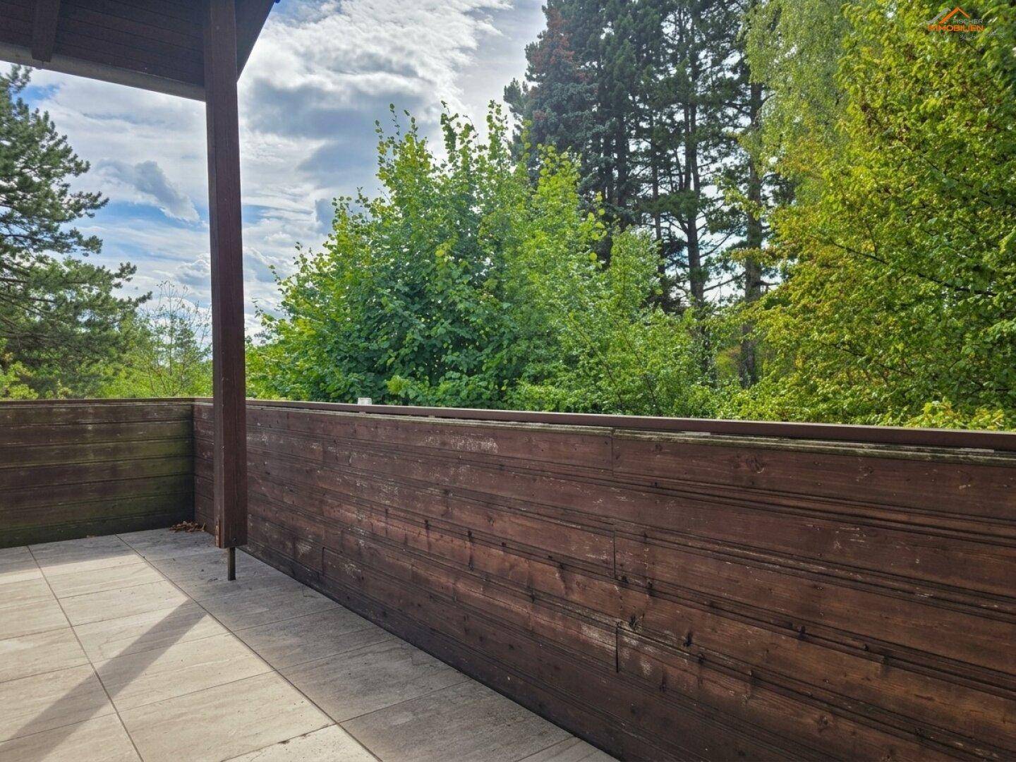 Überdachter Balkon mit Holzwänden und Blick ins Grüne, ideal zum Entspannen.