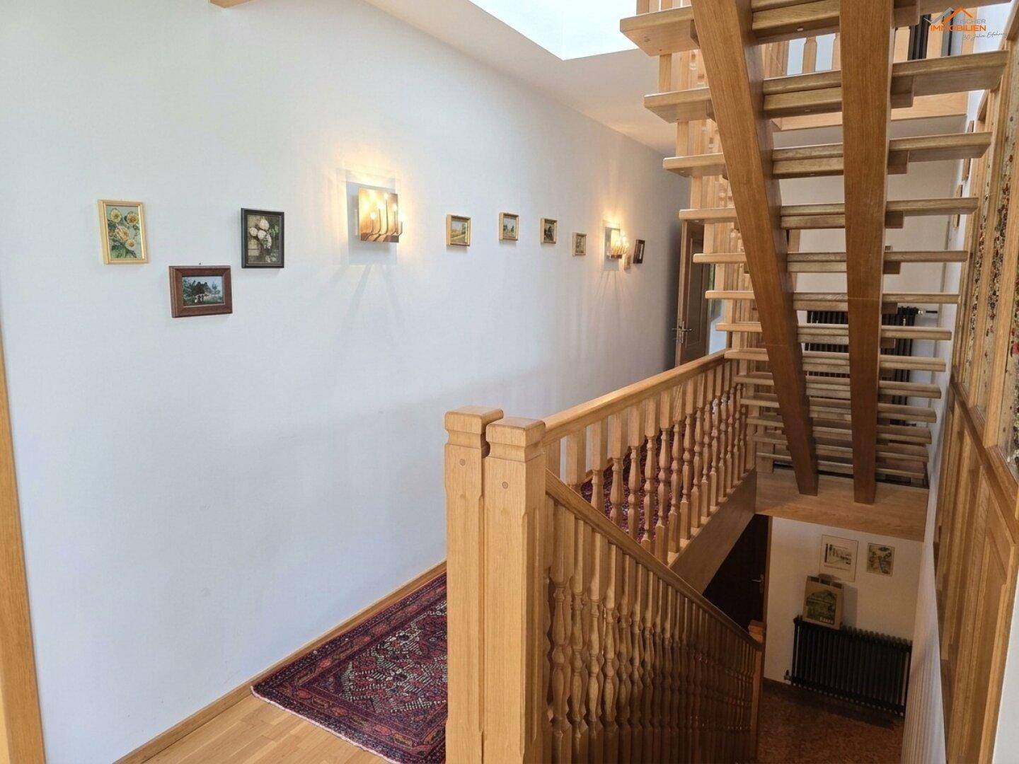 Helles Treppenhaus mit Holzgeländer und Teppichläufer, das die Etagen verbindet.