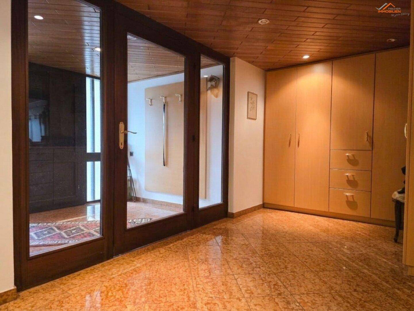Geräumiger Eingangsbereich mit Einbauschränken, Holzdecke und gefliestem Boden.