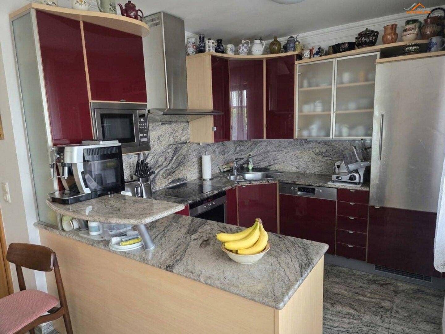 Moderne Küche mit roten Hochglanzfronten, Granitarbeitsplatten und integrierten Geräten.