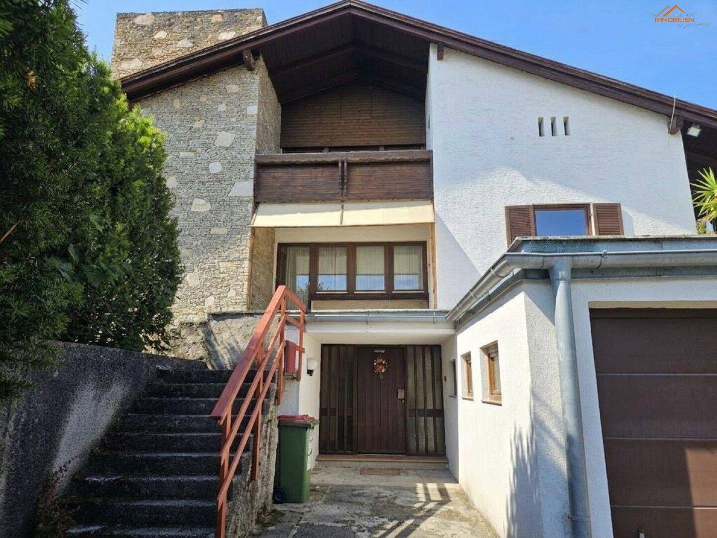 Traditionelles Haus mit Steinfassade, Außentreppe und integrierter Garage im Eingangsbereich.
