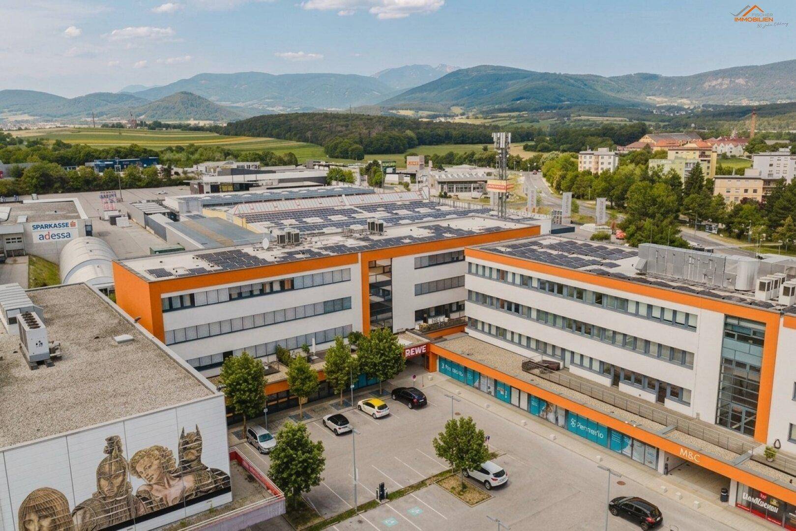 Luftaufnahme eines modernen Geschäftskomplexes mit Solaranlagen auf den Dächern und Bergpanorama.