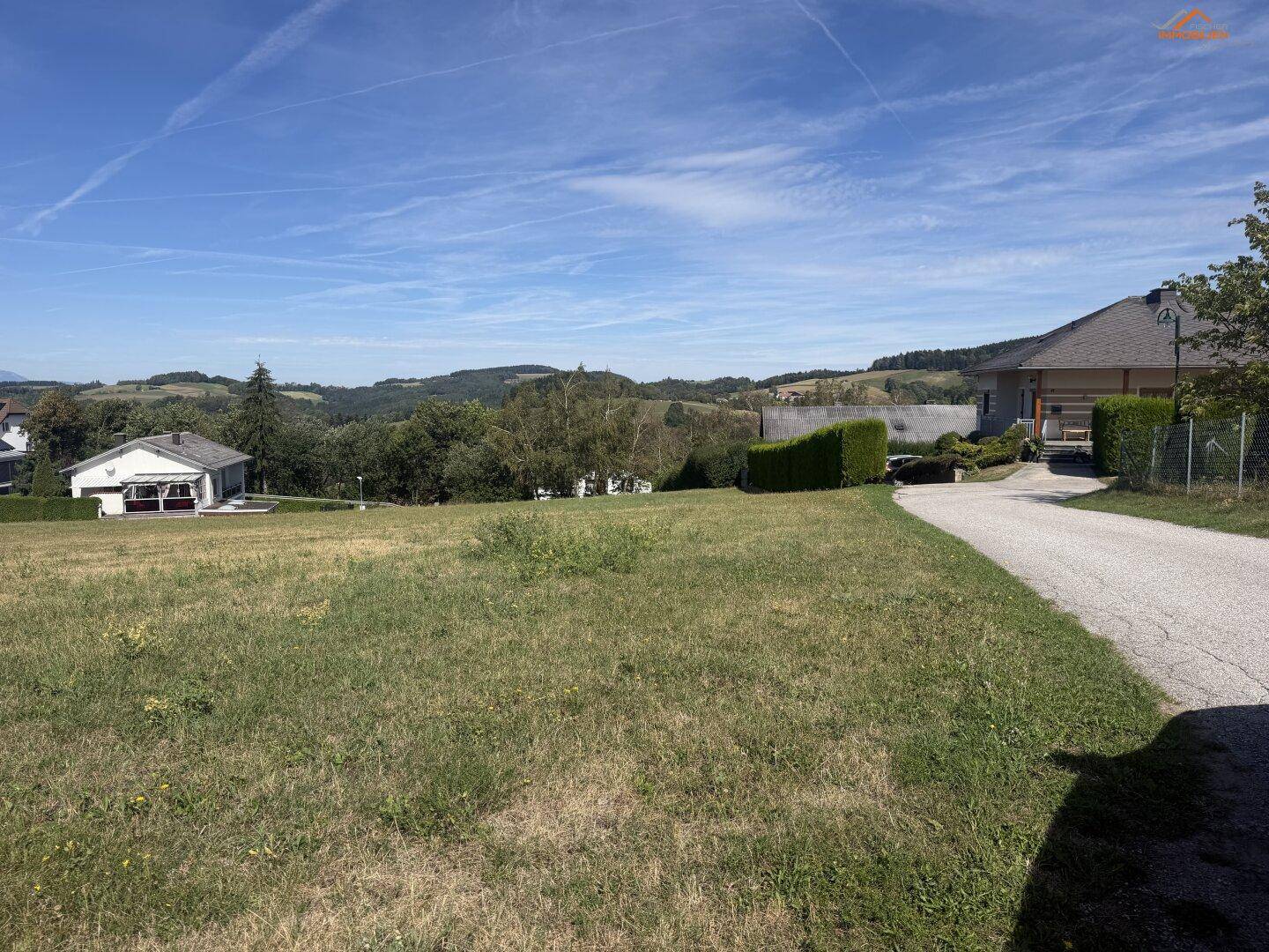 Grünes Baugrundstück mit Zufahrt und Panoramablick auf die sanften Hügel der Umgebung.