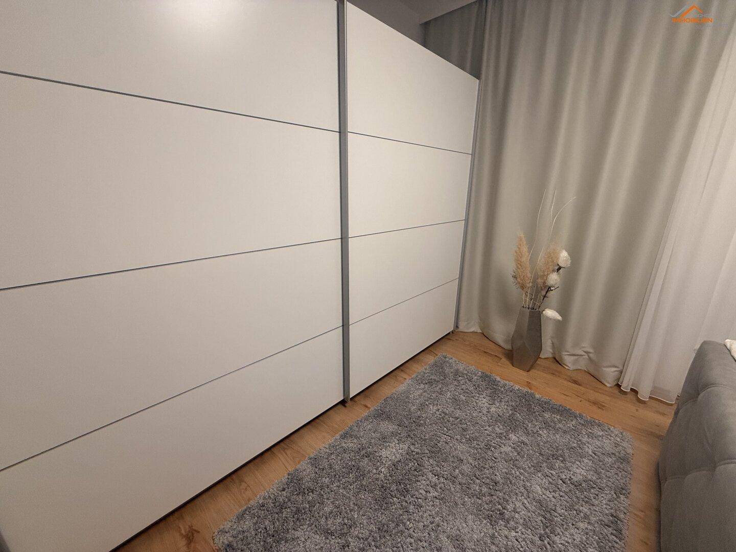 Schlafzimmer mit großem weißen Kleiderschrank, Holzboden und weichem Teppich.