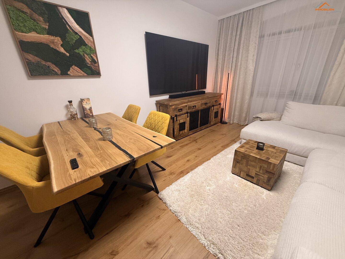 Heller Wohn- und Essbereich mit beigem Sofa, Holztisch und großem Fernseher.