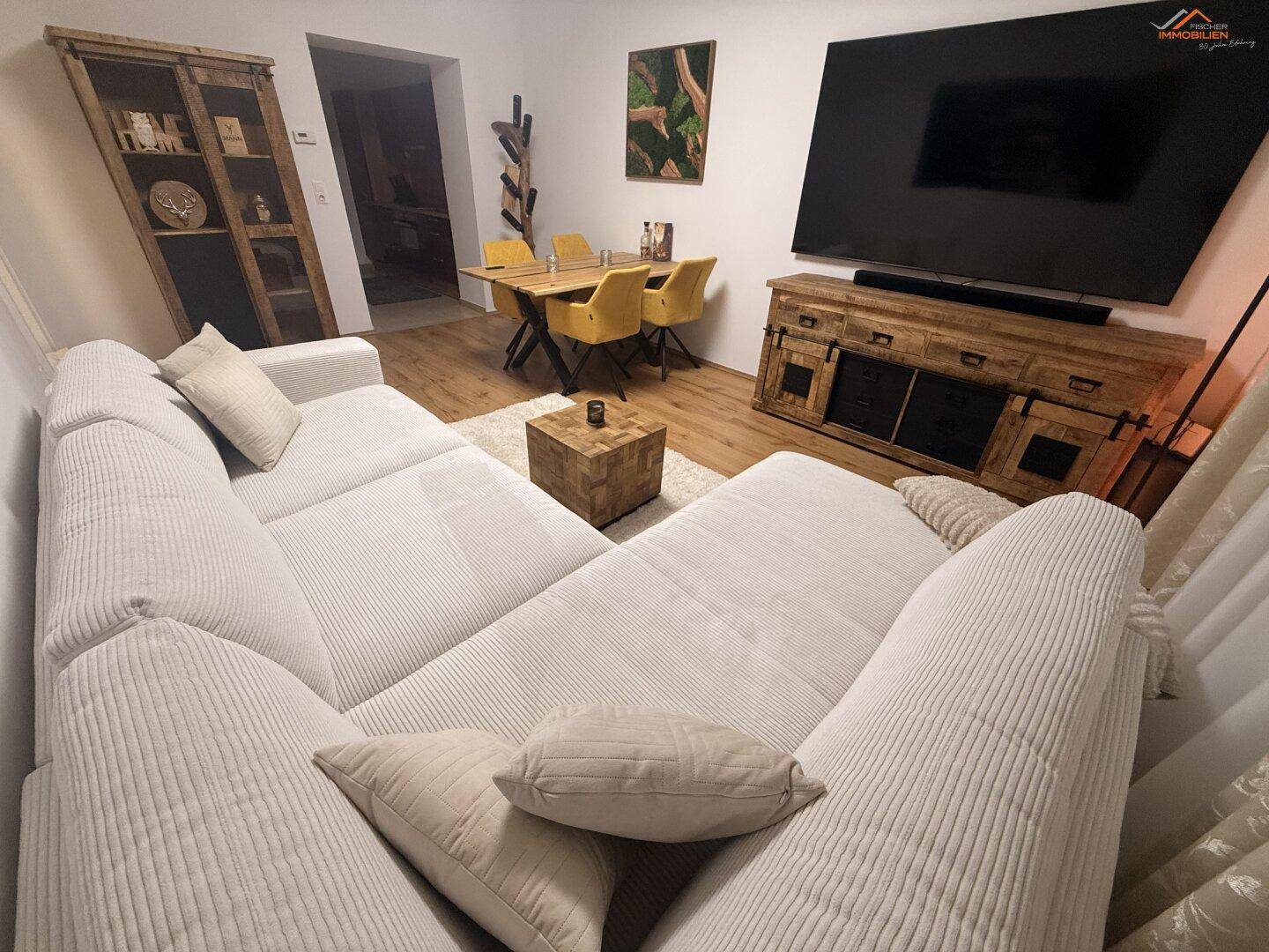 Gemütlicher Wohn-Essbereich mit großem Sofa, Holzboden und modernem Esstisch.