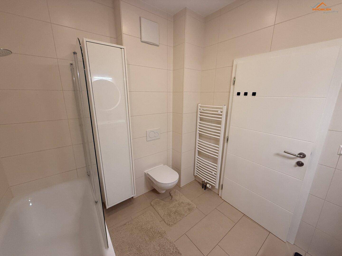 Modernes Badezimmer mit Badewanne, Toilette, Handtuchheizkörper und hellen Fliesen.