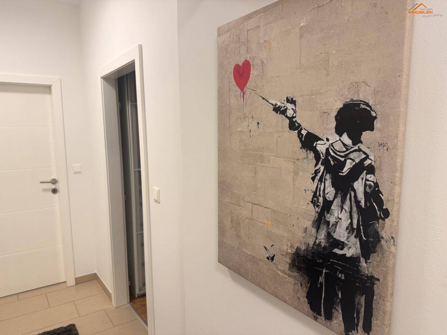 Heller Flur mit modernem Kunstwerk und weißer Tür, führt zu weiteren Räumen.