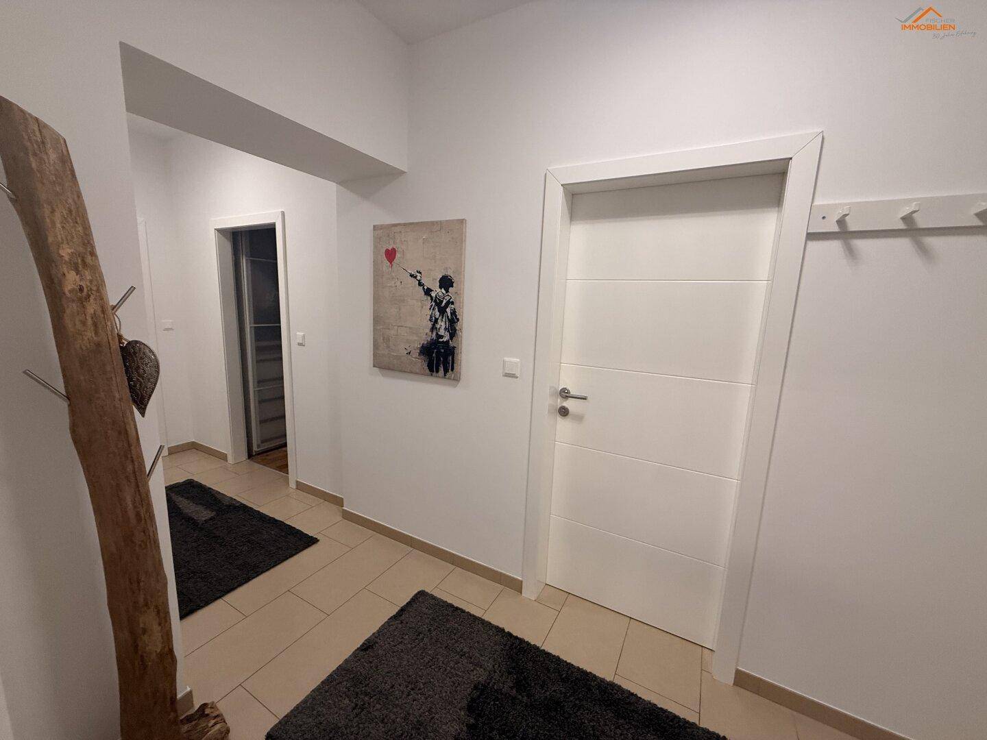 Heller Flur mit Fliesenboden, weißer Tür und modernem Kunstwerk an der Wand.