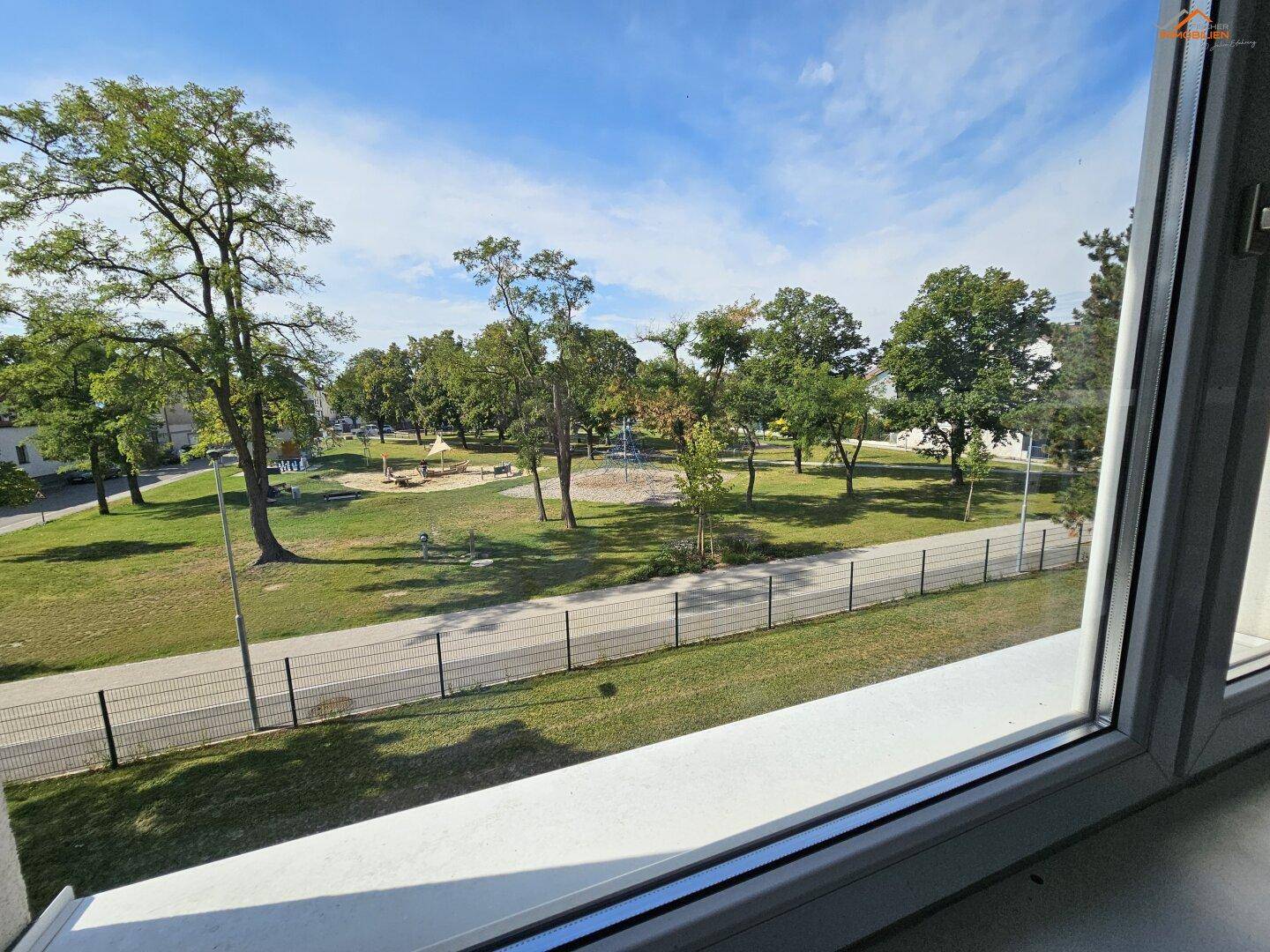 Ausblick aus dem Fenster auf einen grünen Park mit Spielplatz und Bäumen.