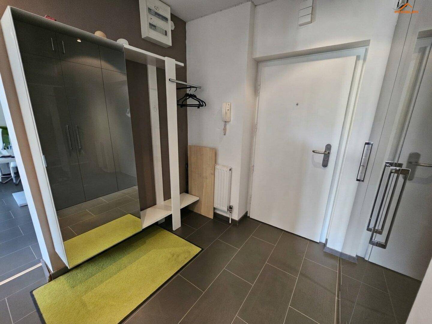Eingangsbereich mit dunklen Fliesen, Garderobe und großem Spiegel.