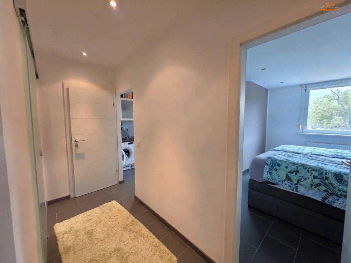 Heller Flur mit dunklen Fliesen, der zu einem Schlafzimmer und einem Hauswirtschaftsraum führt.