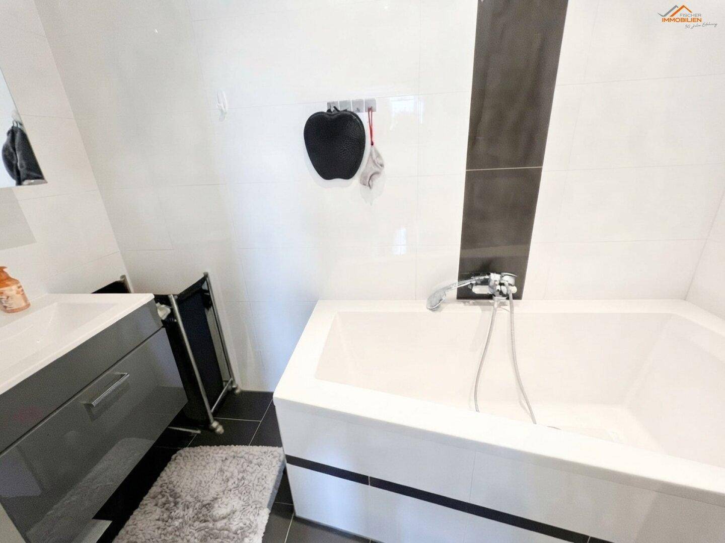 Modernes Badezimmer mit Badewanne, weißen Fliesen und dunklem Akzentstreifen.