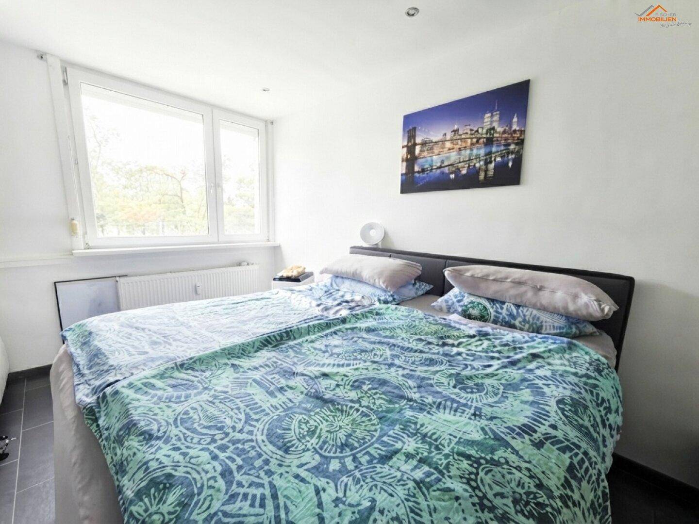 Helles Schlafzimmer mit Doppelbett, großem Fenster und schlichter Dekoration.