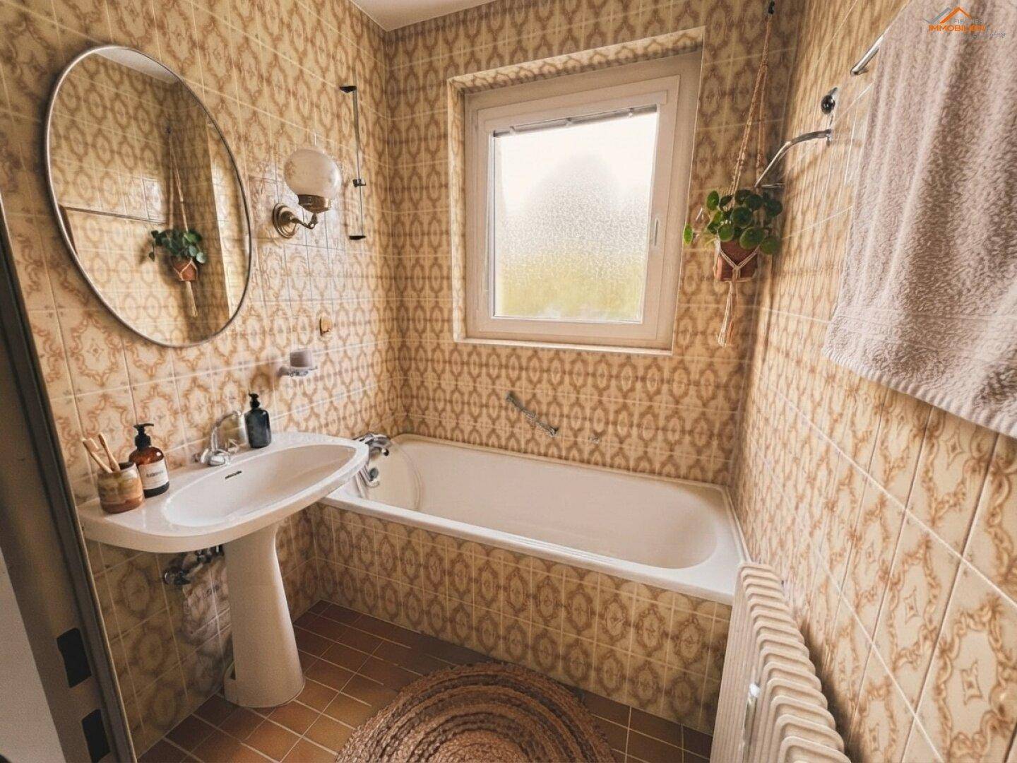 Badezimmer mit gemusterten Fliesen, einer Badewanne und einem Fenster für Tageslicht.