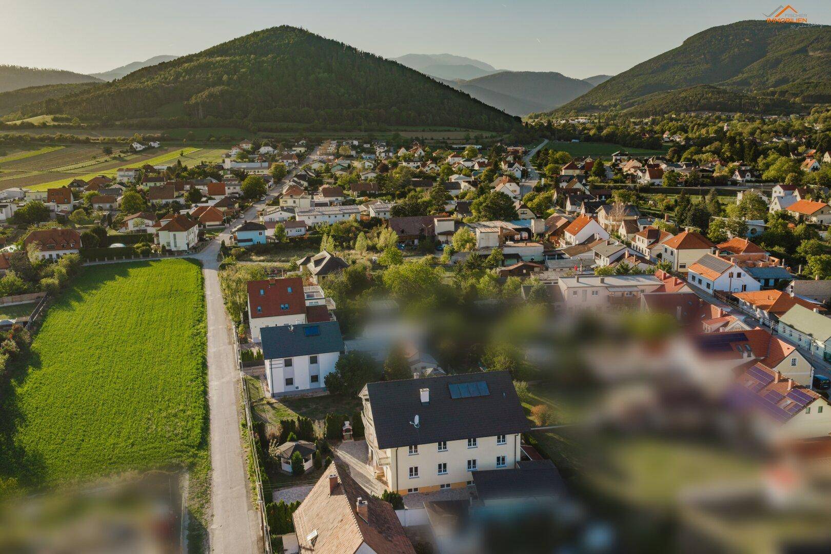 Luftaufnahme eines Hauses in ländlicher Umgebung mit weitem Blick auf grüne Berge.