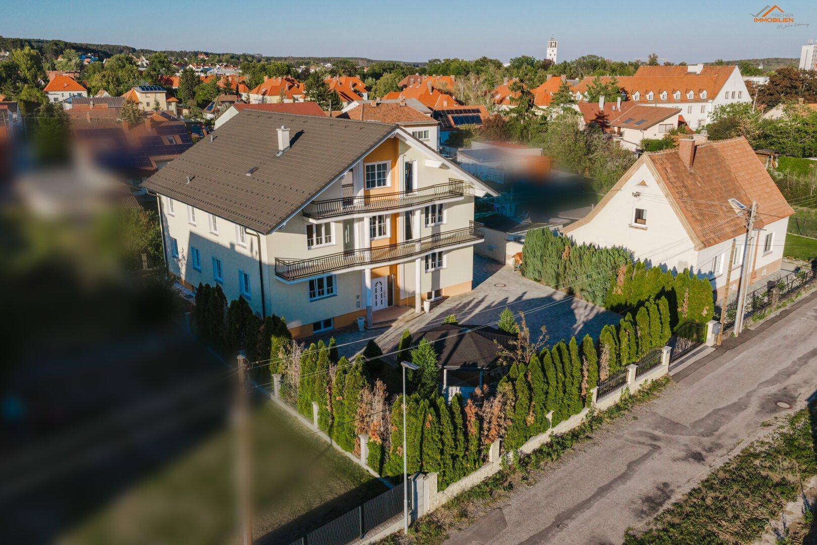 Luftaufnahme eines großen Wohnhauses mit mehreren Balkonen und einem gepflegten Vorgarten.