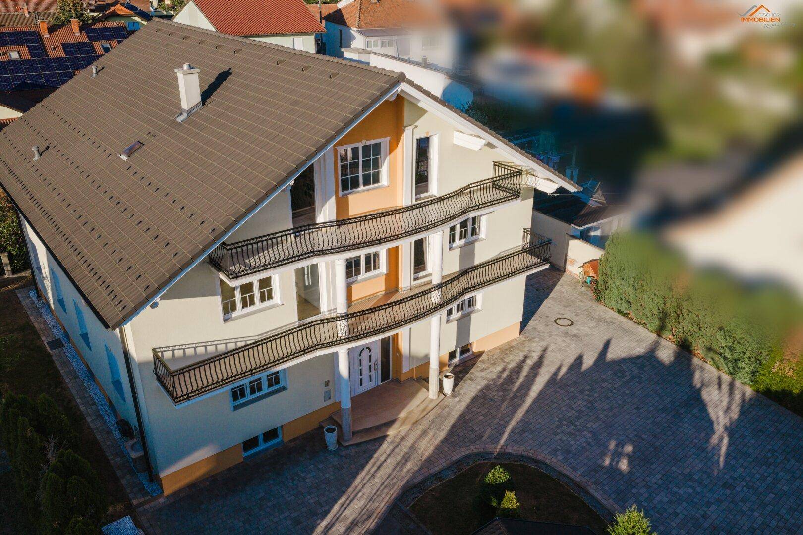 Ansicht des Hauses von oben mit mehreren Balkonen, gepflasterter Auffahrt und gepflegter Fassade.