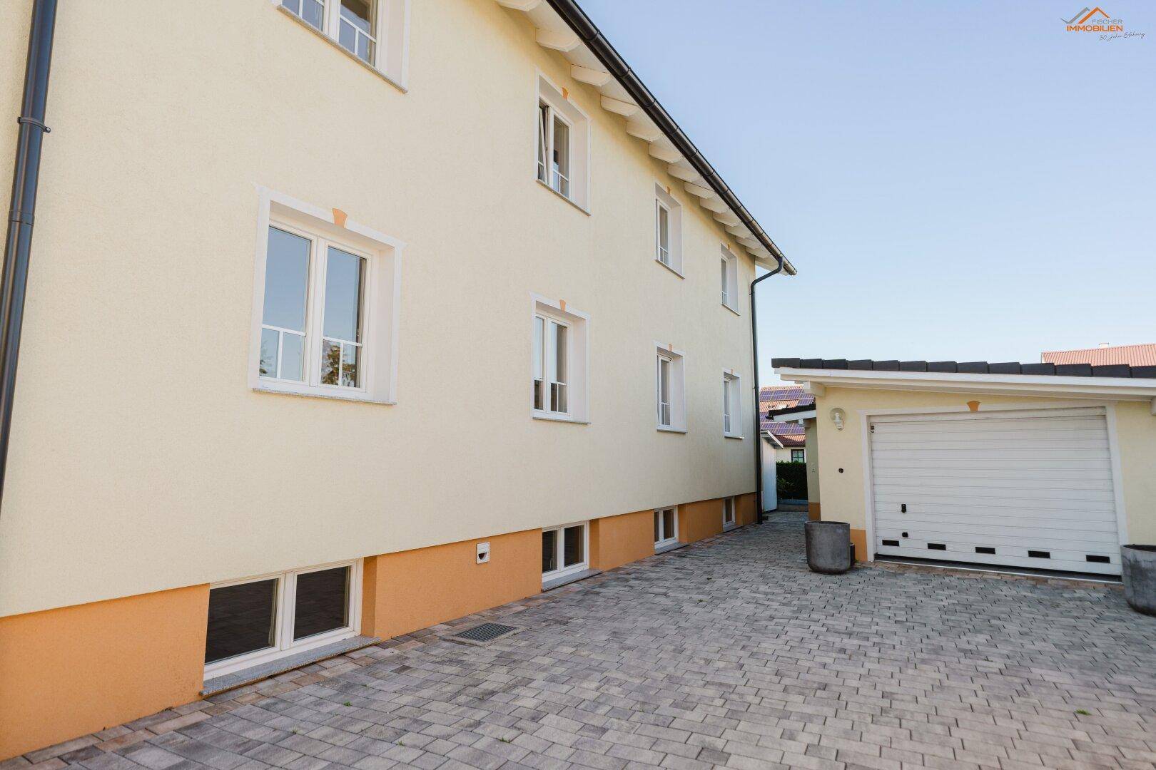 Seitenansicht des Hauses mit Garage, gepflasterter Zufahrt und mehreren Fenstern im Untergeschoss.
