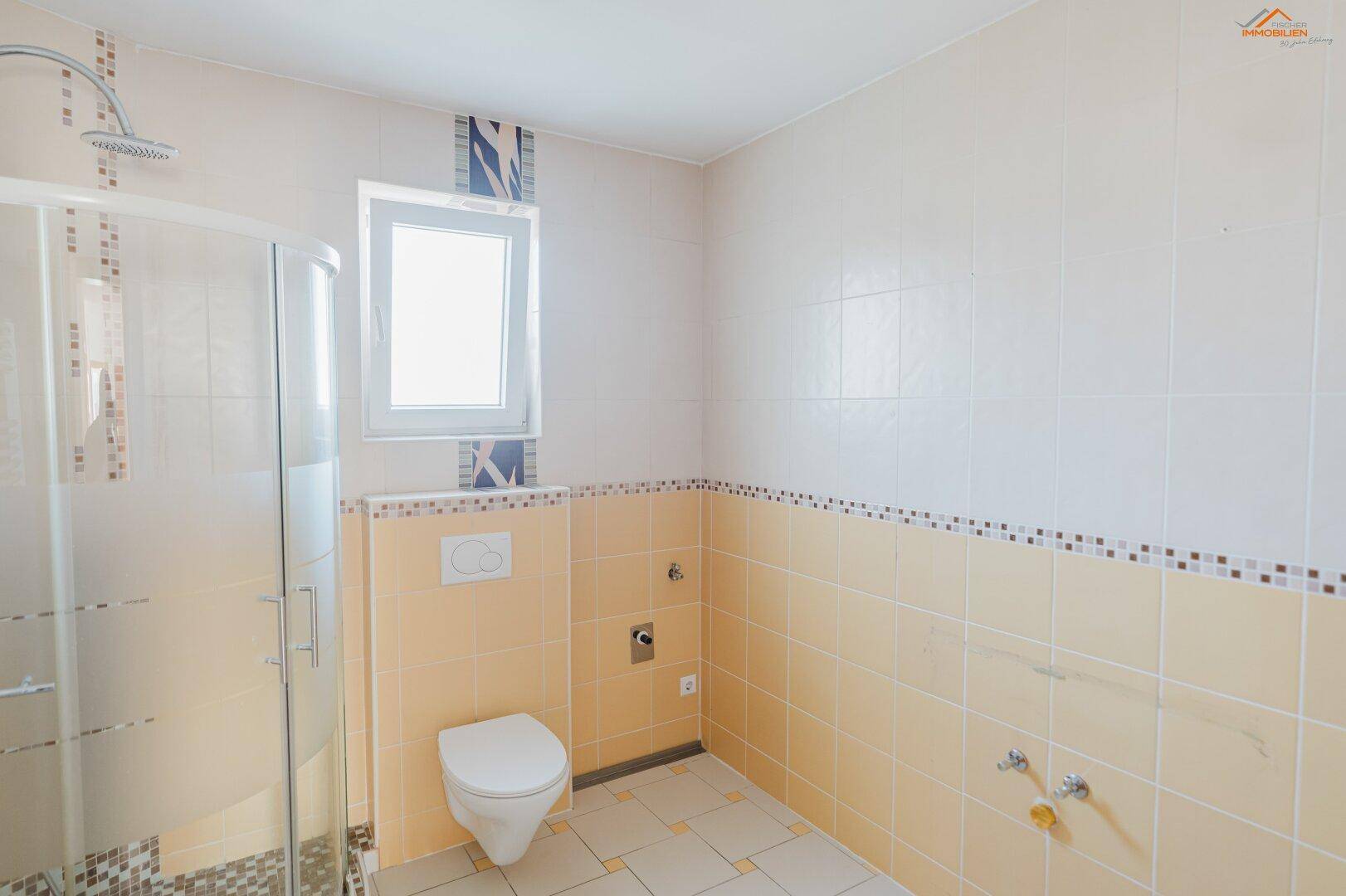 Helles Badezimmer mit Duschkabine, Wand-WC und beigefarbenen Fliesen.